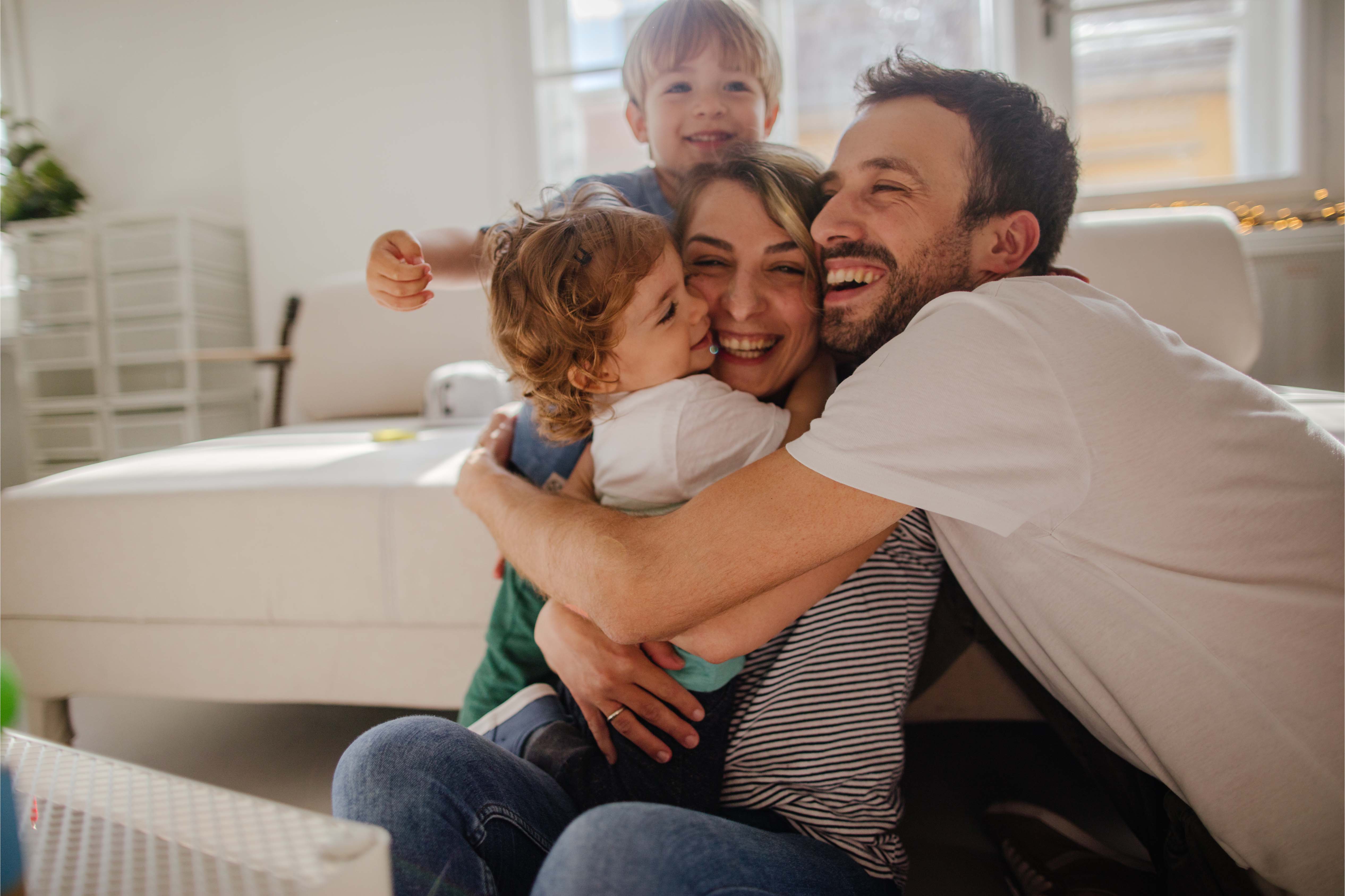 Family of four hugging on a sofa at home, smiling and relaxed