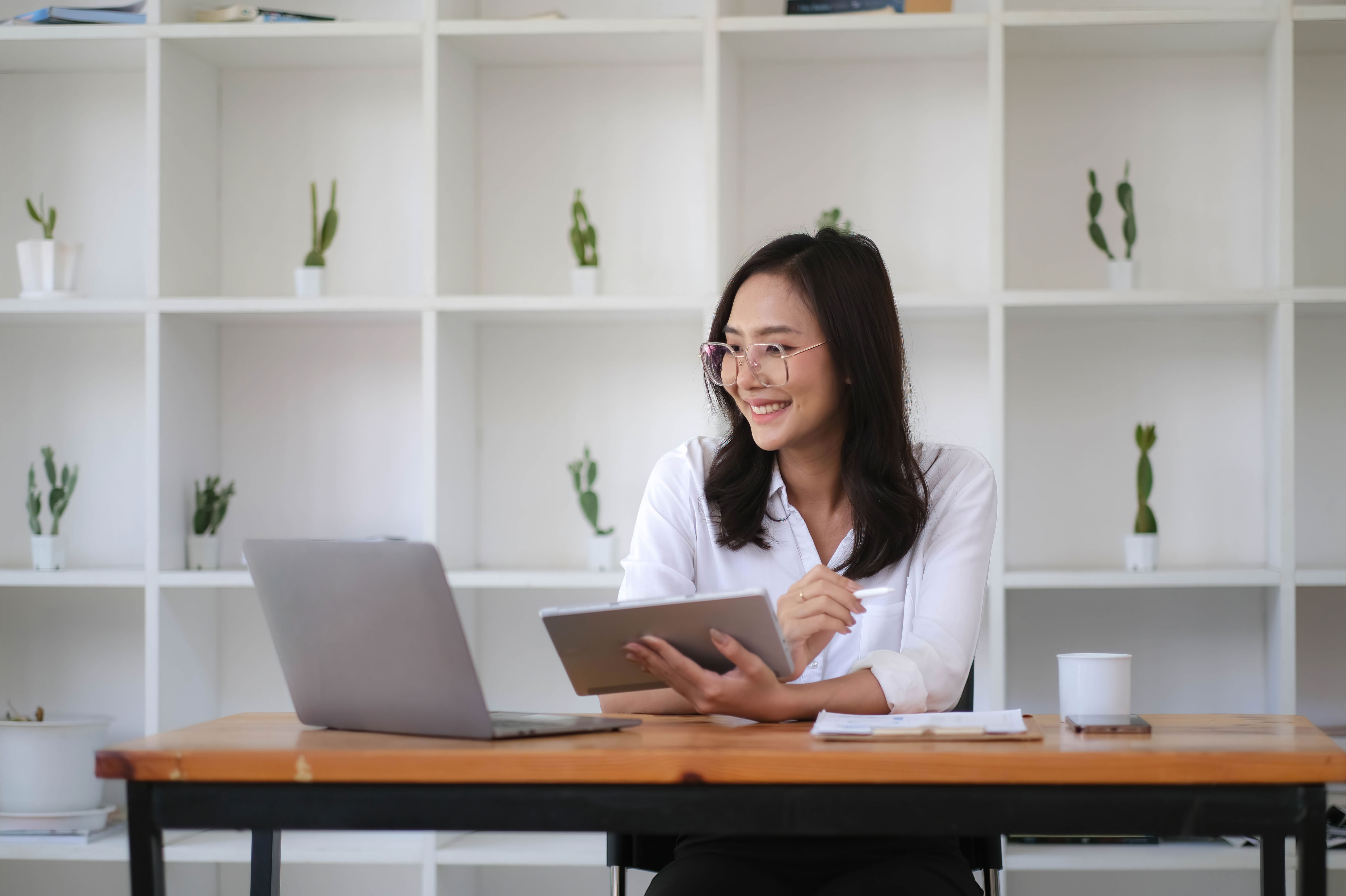 Smiling professional woman working with a tablet and laptop in a modern Thai office