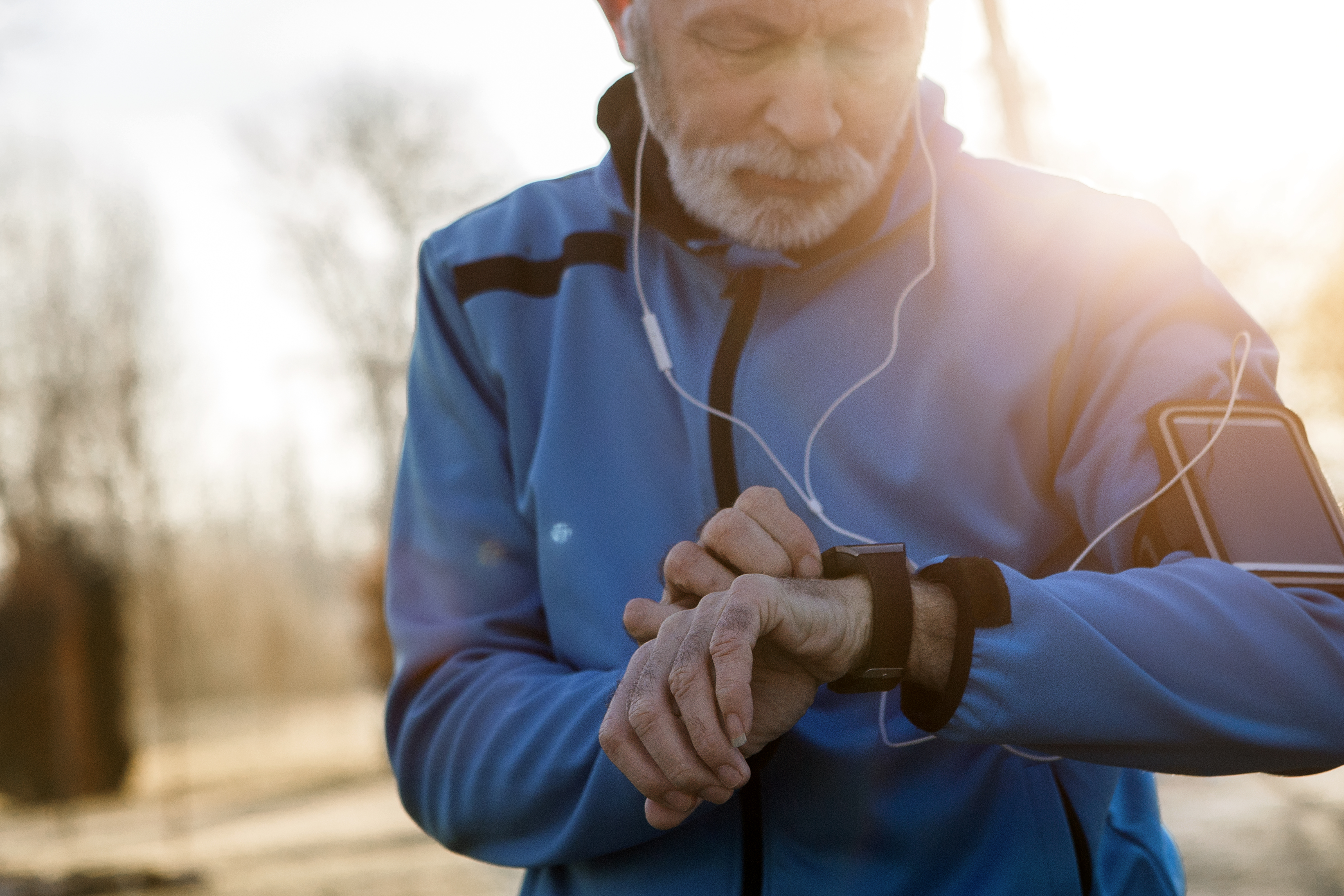 An older man checks his activity monitor while out running through sunny woods
