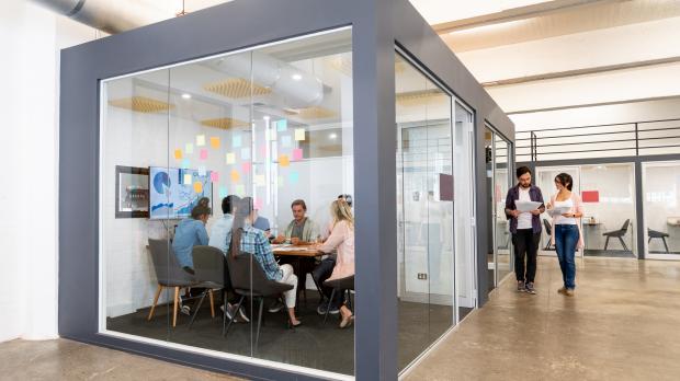 A group of business people sit at a board meeting in a glass-walled room