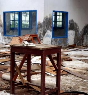 A white landline phone sits on a table in a ruined building, surrounded by rubble