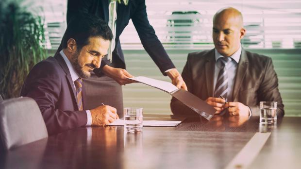 Merger being signed by two guys at a boardroom table