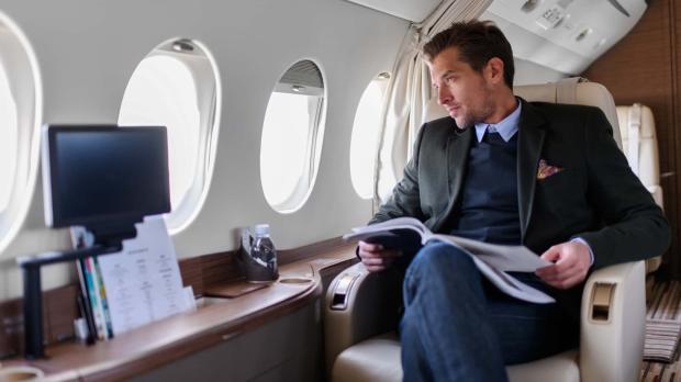 A suave gentleman in a tailored suit looks out of the window of his private jet