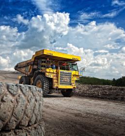 A yellow dumper truck drives down a road against a blue sky