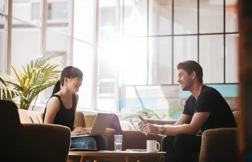 Two young professionals smile together in a modern, bright office