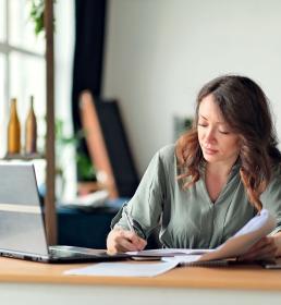 Woman writing at desk in front of laptop