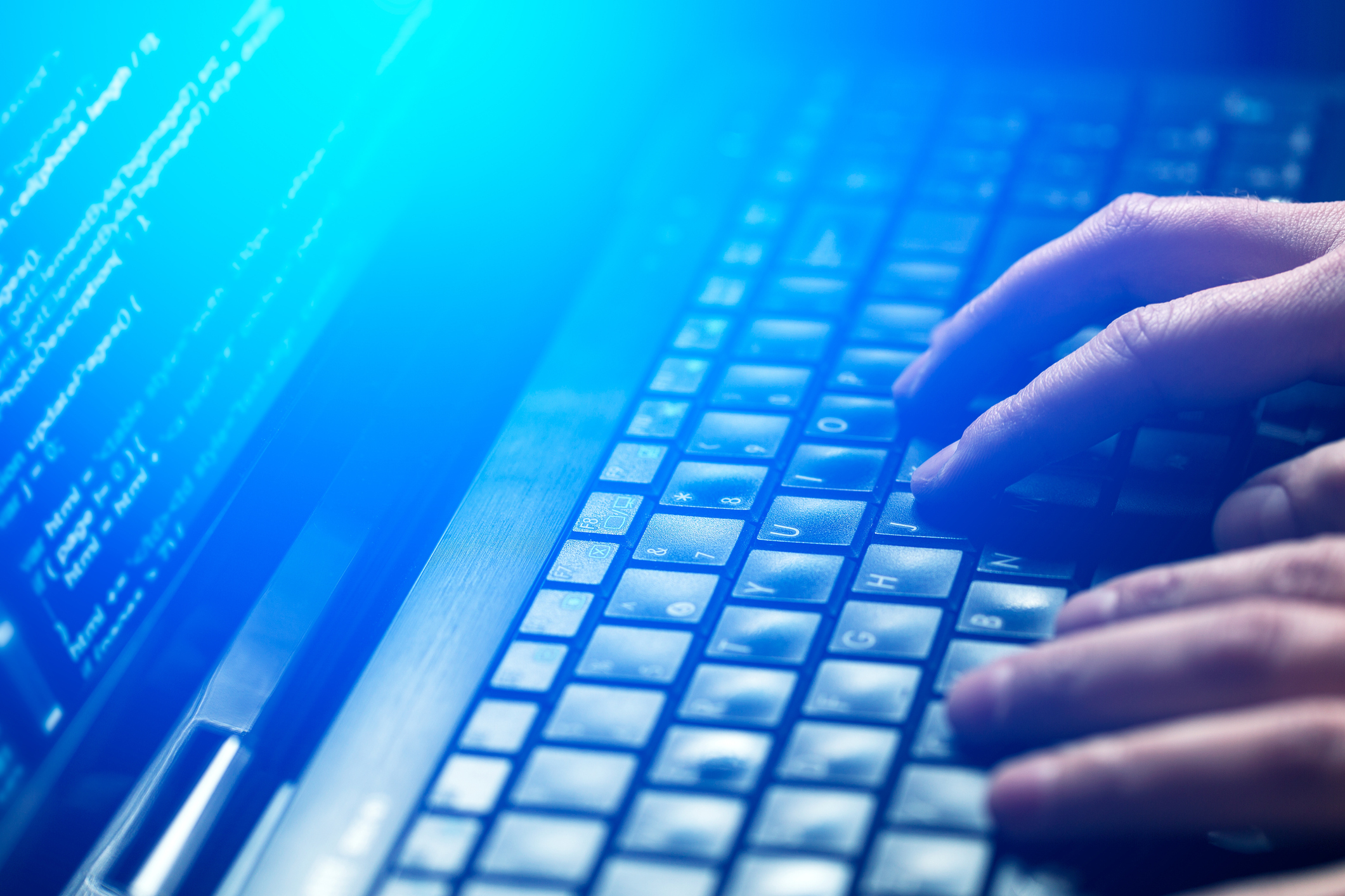 Hands type on a keyboard in front of a computer screen showing code