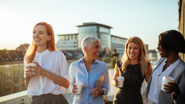 four female collegues drinking coffee and chatting laughing