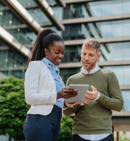 two people outside talking while looking at a tablet