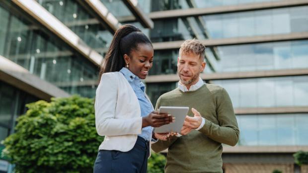 two people outside talking while looking at a tablet