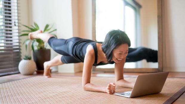 Woman doing yoga while looking at a laptop Woman doing yoga while looking at a laptop