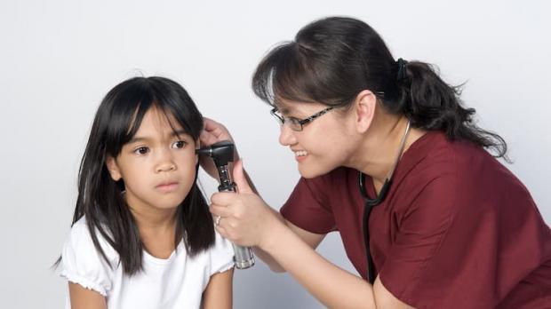 Doctor taking temperature in young girl's ear