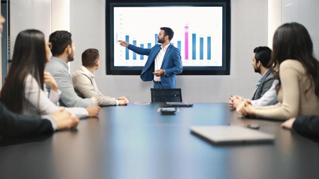 Financial advice presentation man showing graph to table full of people Financial advice presentation man showing graph to table full of people