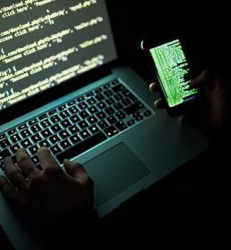 A computer hacker working on a laptop and a smartphone