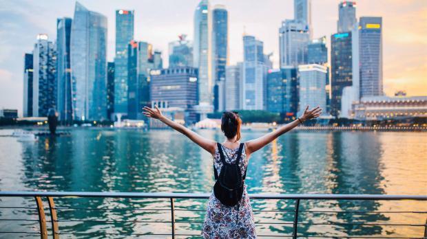 Celebrating Singapore’s Skyline Person with arms raised looking at Singapore’s Marina Bay skyline at sunset, symbolising opportunity and growth