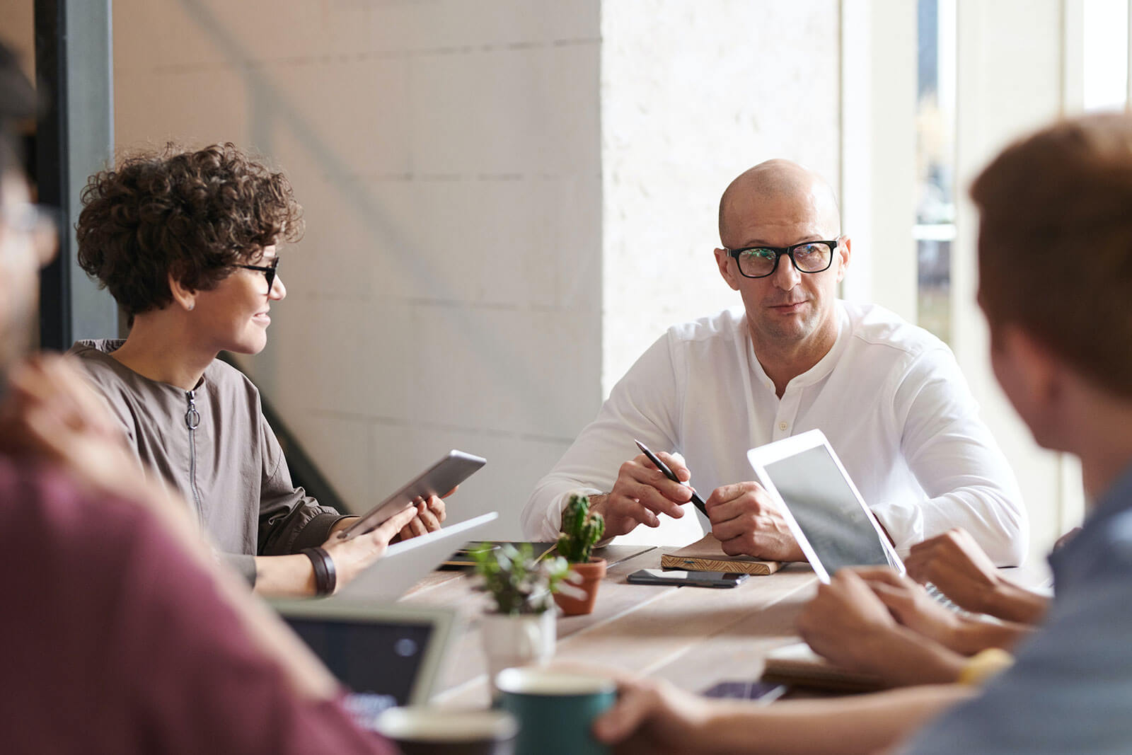 Business team meeting in modern office with professionals using tablets and laptops, corporate collaboration, project discussion, and workplace communication.