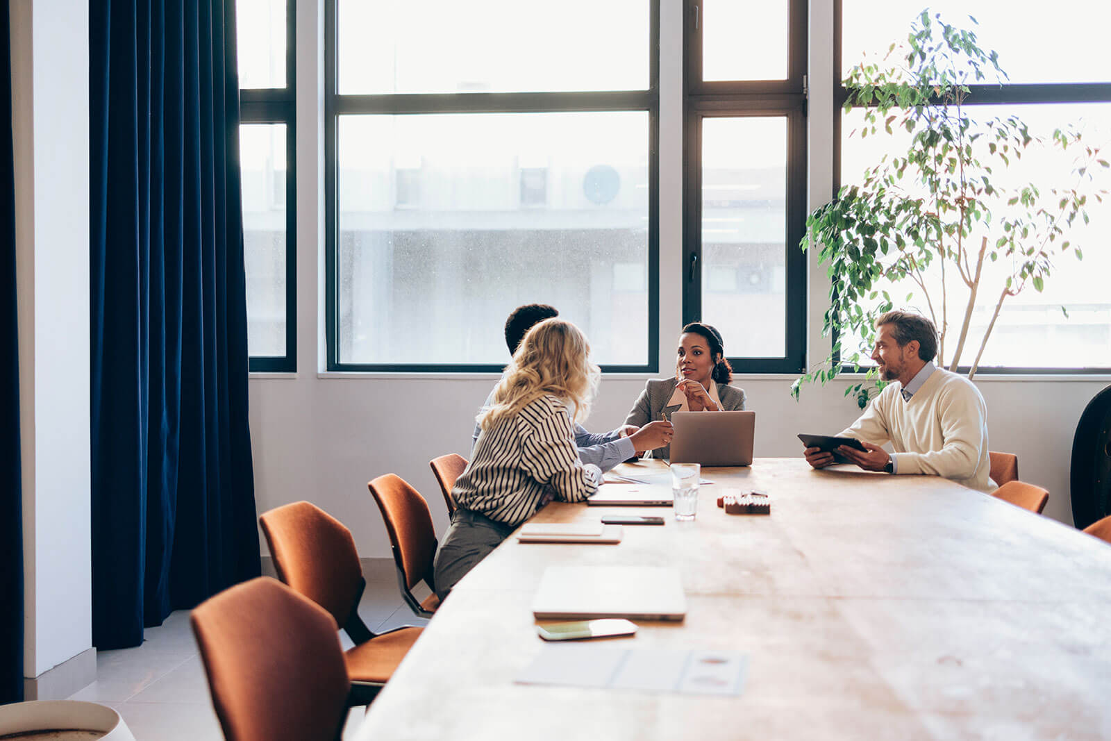 Corporate team meeting in modern conference room with professionals collaborating on laptops and tablets, business strategy discussion, and workplace teamwork.