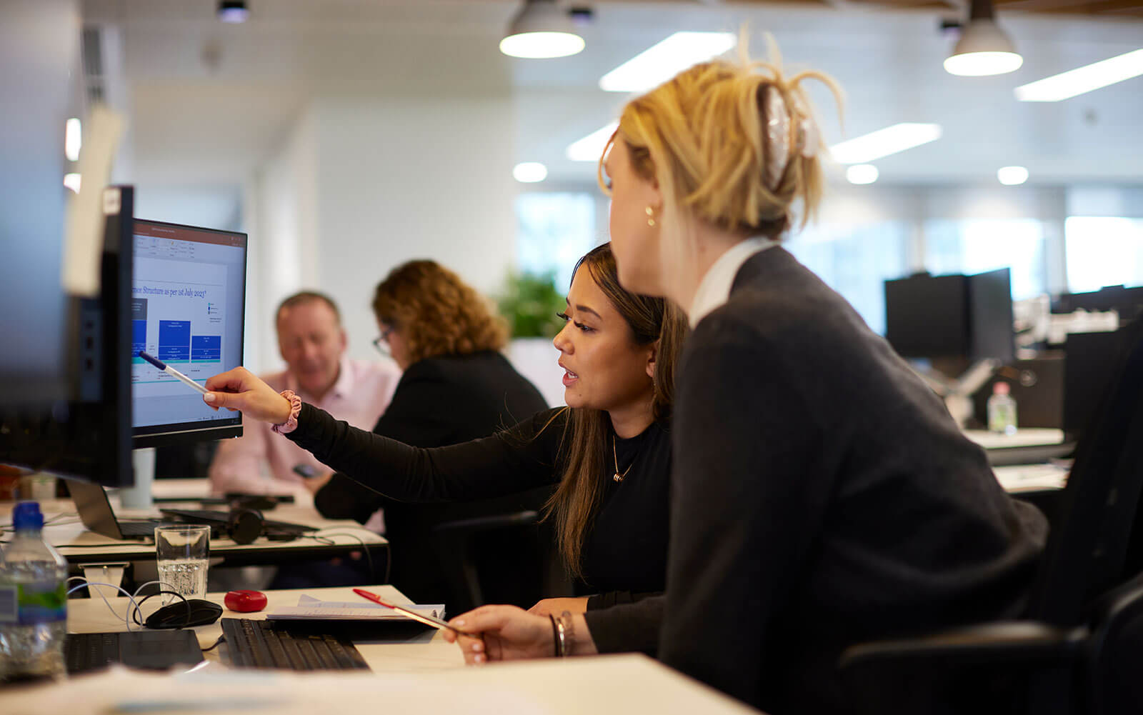 Business professionals reviewing data on computer monitor during office meeting, workplace collaboration, team strategy discussion, and corporate project analysis.
